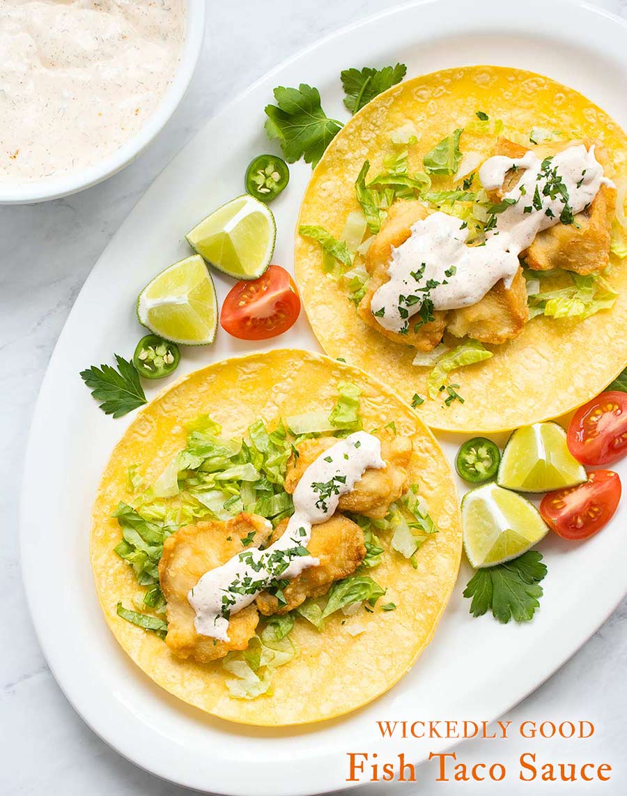 Two San Diego-style fish tacos on a white platter topped with fish taco sauce