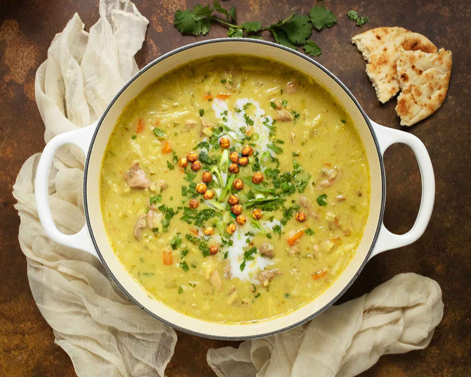 Overhead view of Mulligatawny Soup in a large white Dutch oven with naan on the side.
