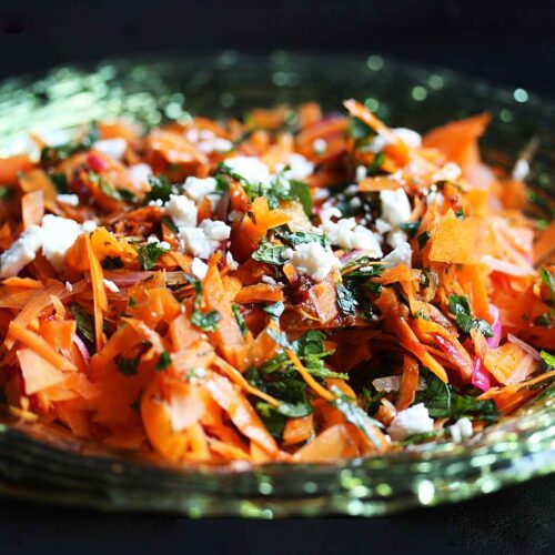 Side angled view of Carrot & Harissa Salad. in a green glass bowl.