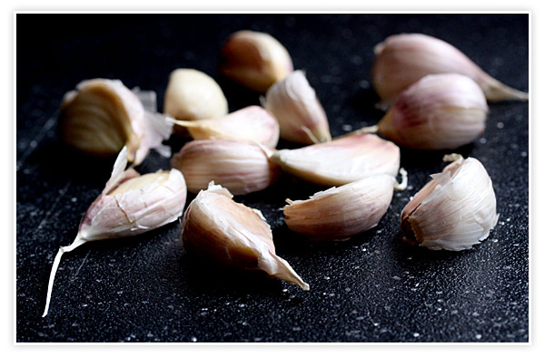 12 cloves of garlic on a black cutting board.
