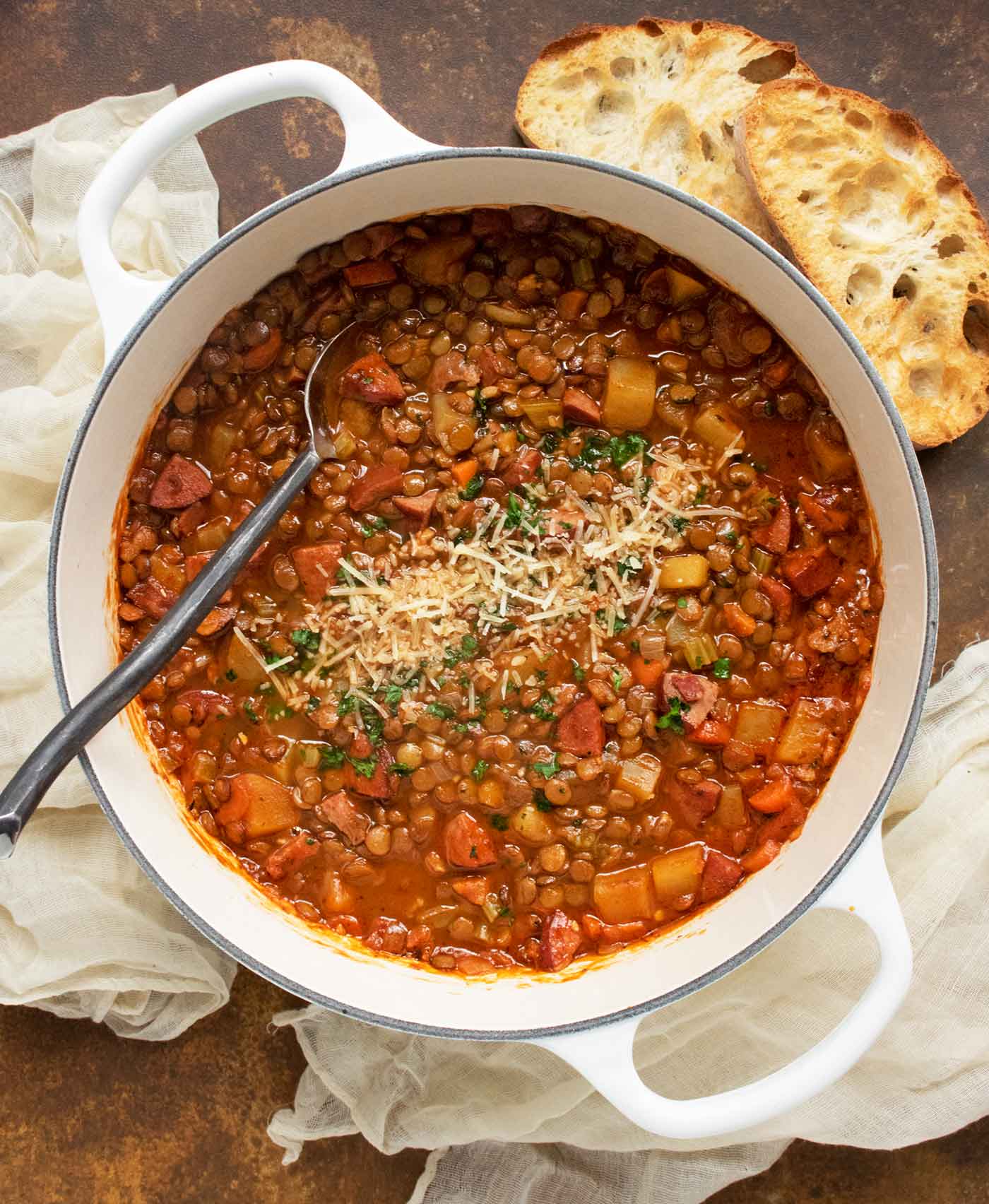 View from above of Rustic Lentil Soup in a large Dutch oven with a serving spoon.