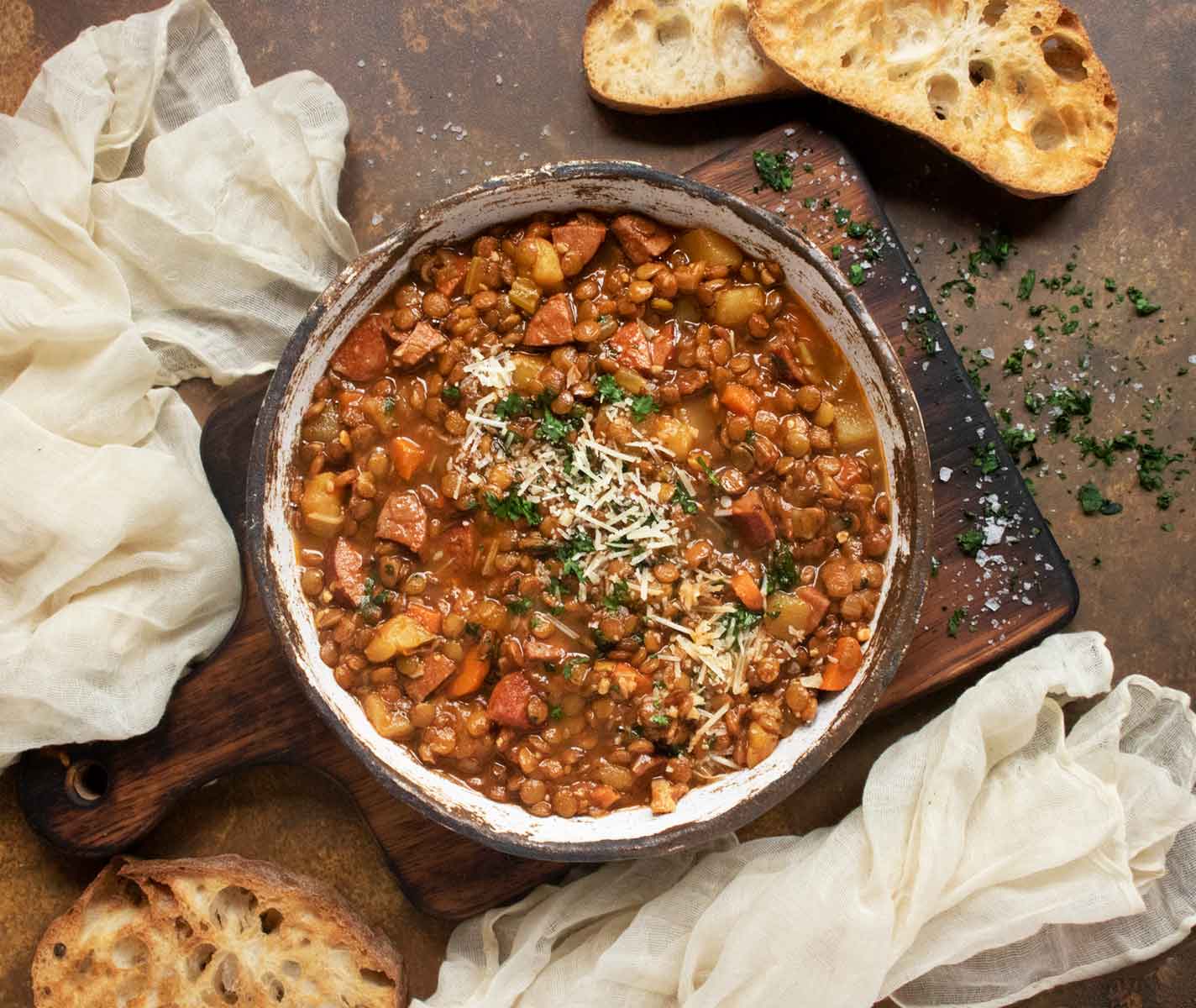 Rustic Lentil Soup in a bowl on a wooden serving board with bread on the side.