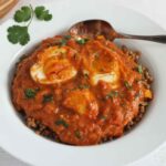 Close-up of egg curry in a white bowl with a spoon.