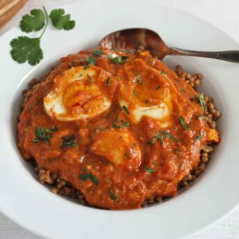 Close-up of egg curry in a white bowl with a spoon.