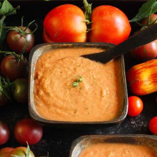 Guaczpacho in a square bowl surrounded by tomatoes