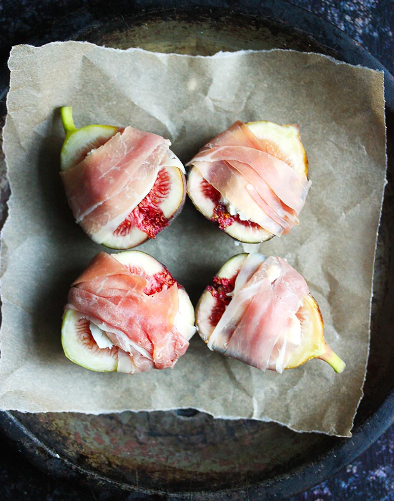 Figs on a pie tin, stuffed with goat cheese and wrapped with prosciutto, ready to go into the oven.