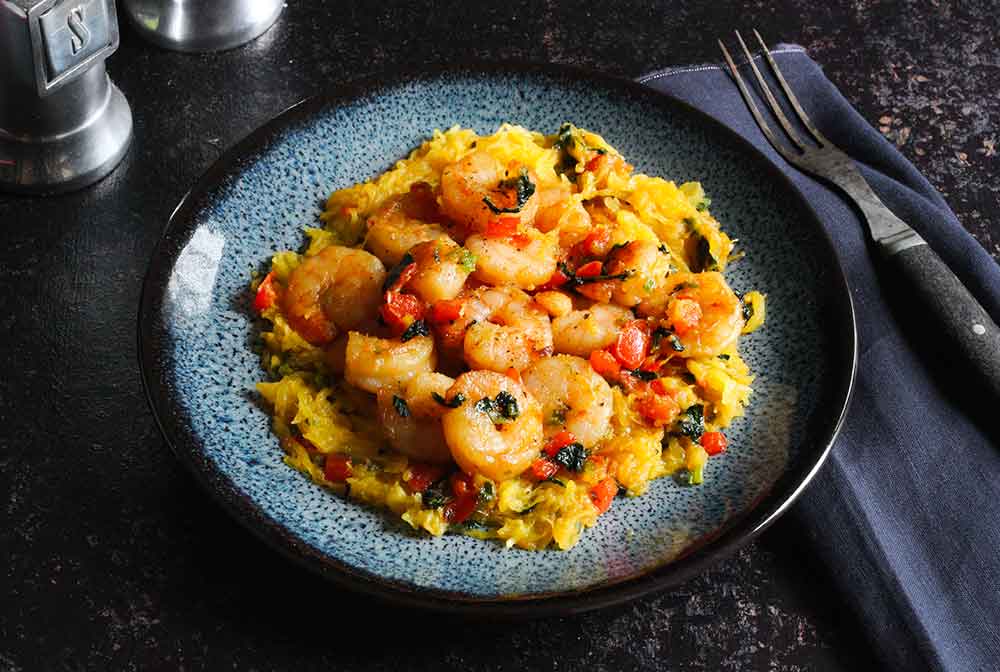 A plate of sauteed shrimp and vegetables over spaghetti squash.