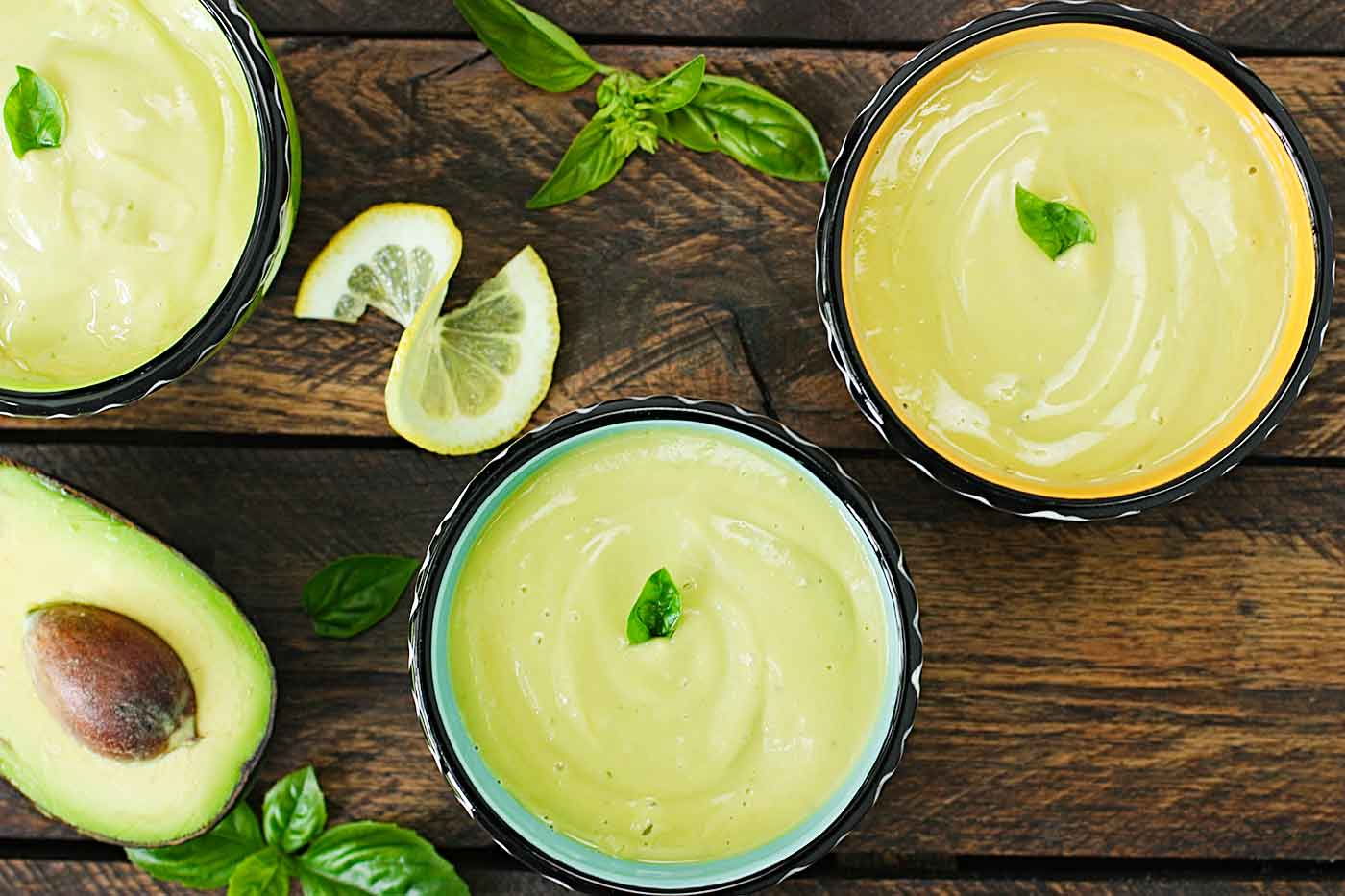 Three bowls of lemon basil avocado soup on a wooden table