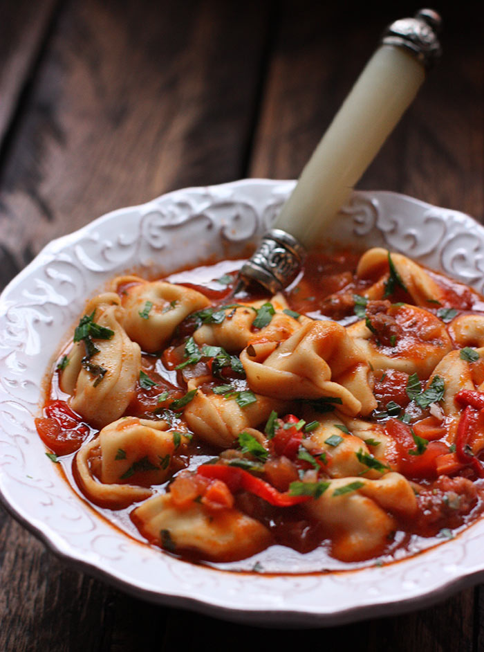 Side view of Italian Tortellini Soup in a white bowl with a spoon.