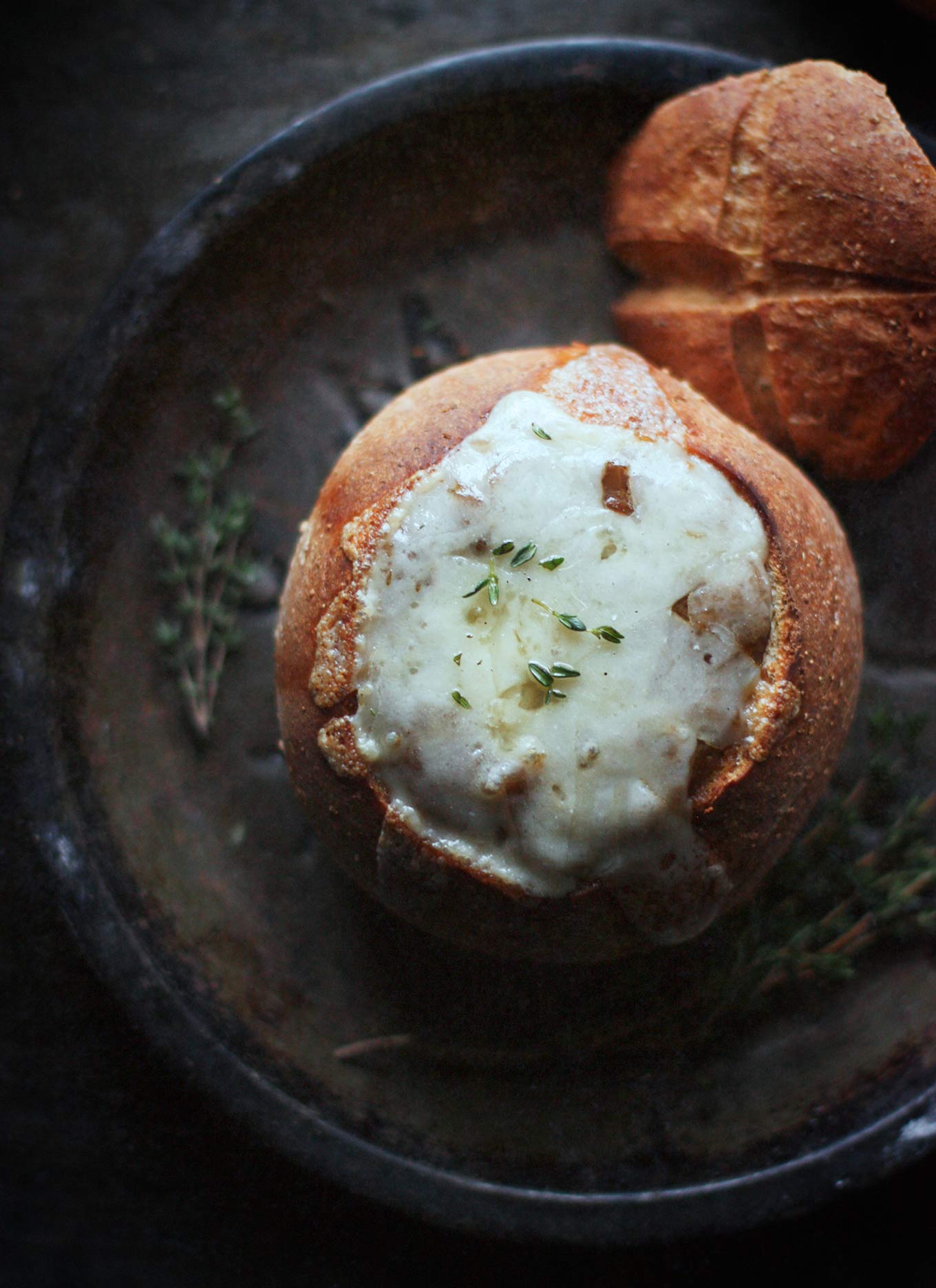 An overhead view of Vegetarian French Onion Soup in a bread bowl with the bowl's cap on the side.