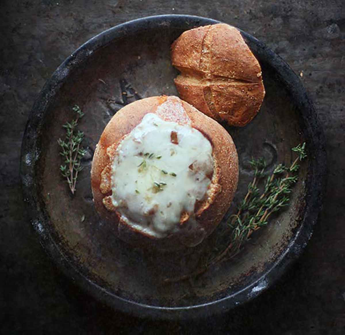 An overhead view of Vegetarian French Onion Soup in a bread bowl, capped with melty cheese.