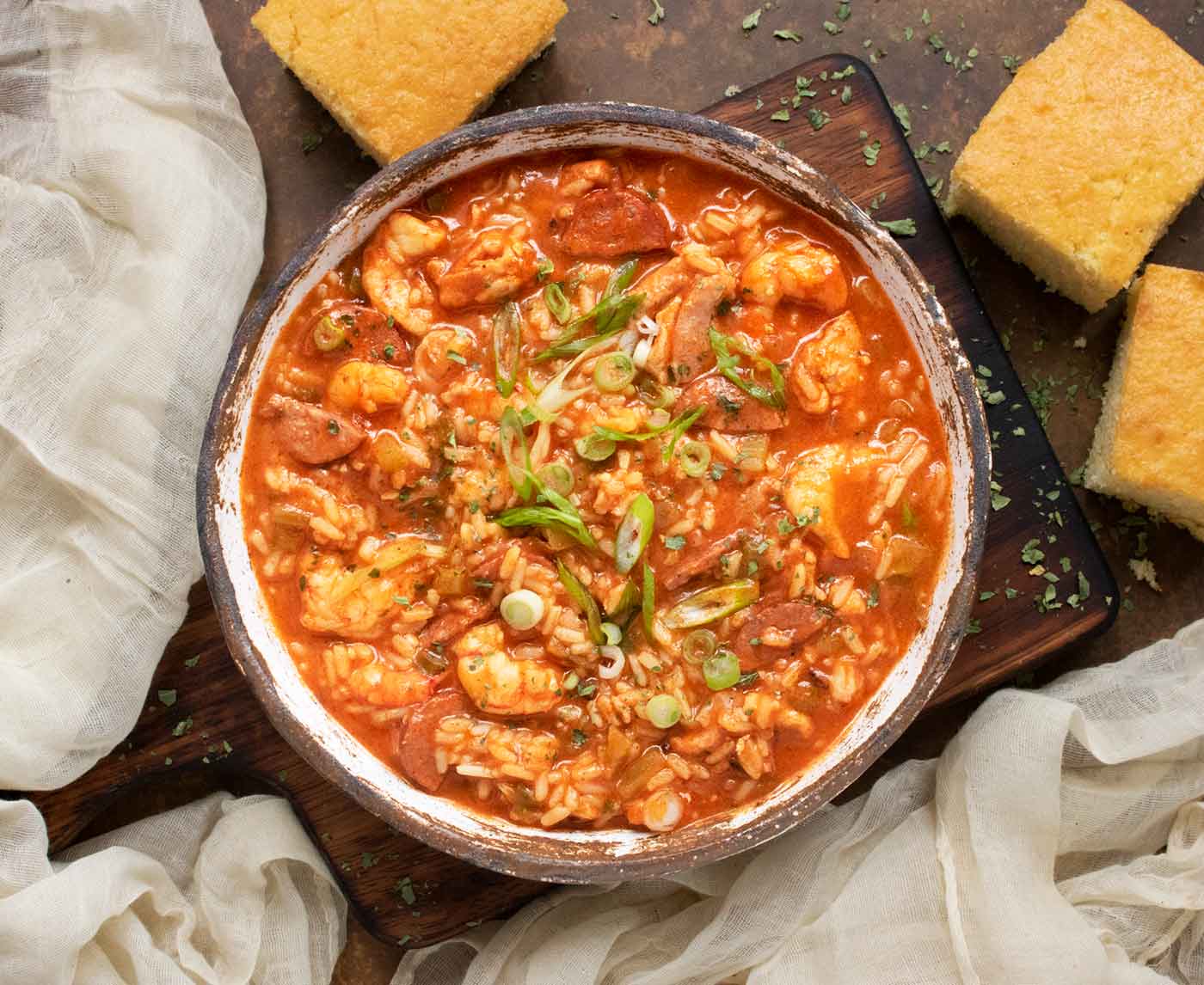 Overhead view of a bowl of Jambalaya Soup on a wooden serving board with cornbread on the side.