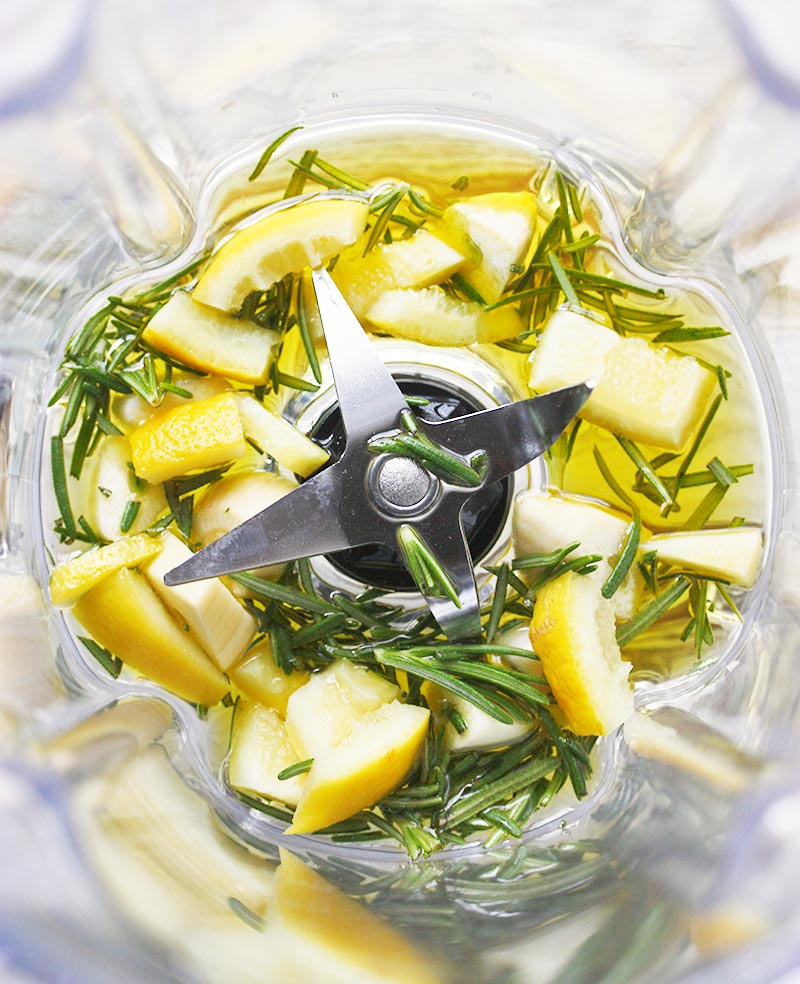 Close up of preserved lemons and herbs in the bottom of a blender jar.