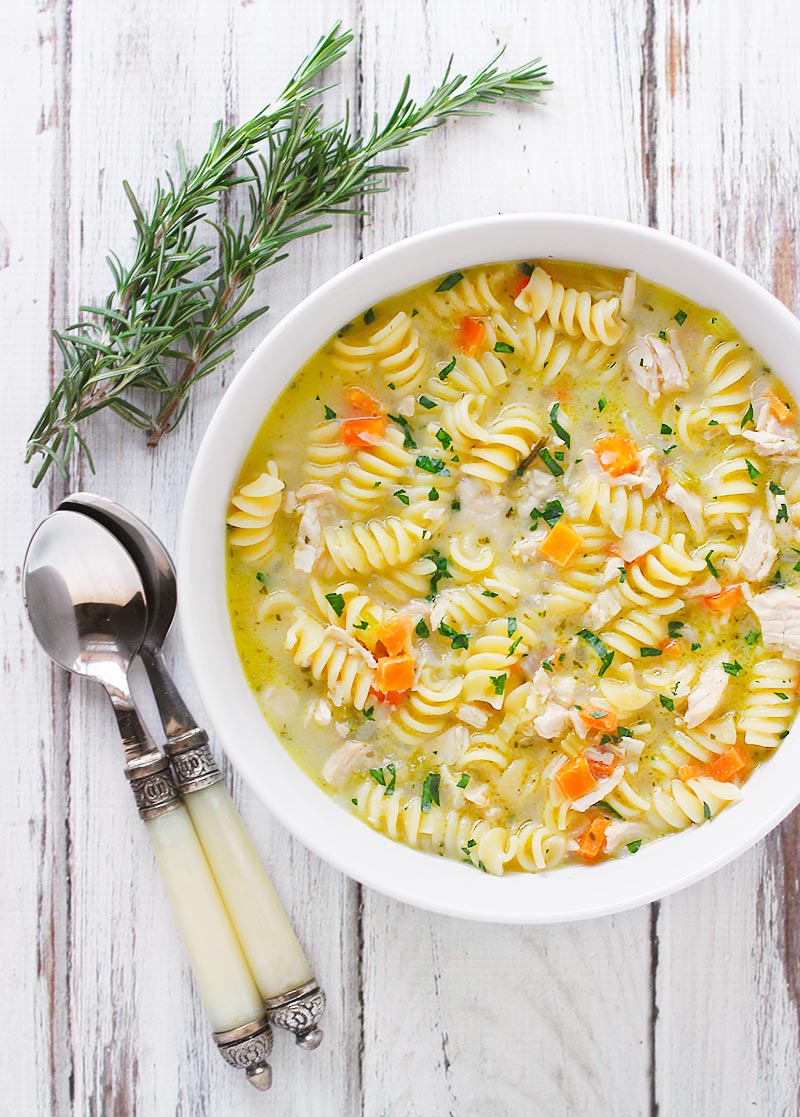 Close-up of a bowl of the soup, with spoons and a sprig of rosemary on the side.