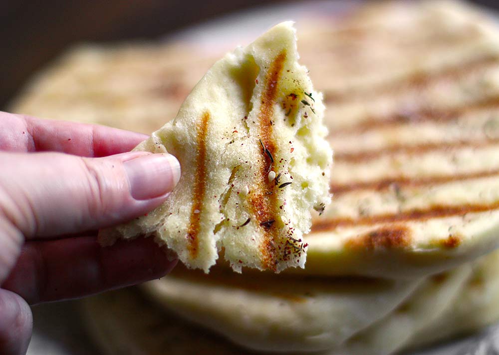 Closeup of my hand holding a piece of the grilled flatbread.