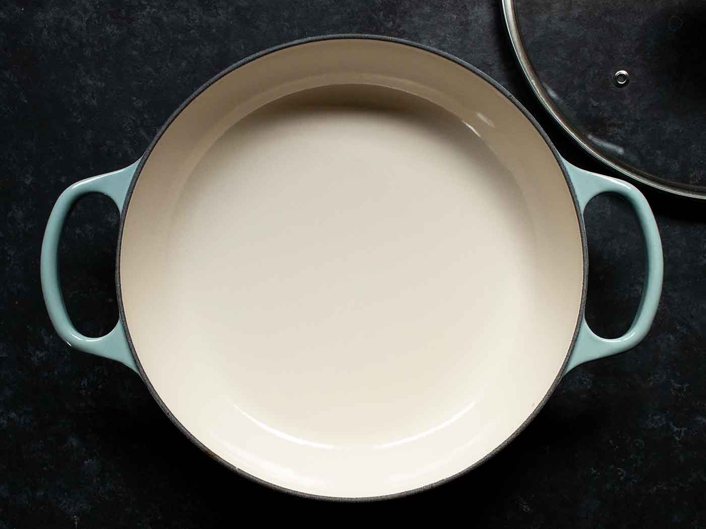 Le Creuset enameled cast iron braiser with sea salt blue handles, glass lid off to the side.