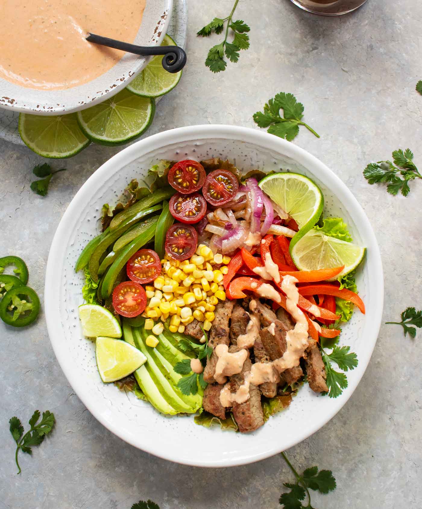 Overhead view of Steak Fajita Salad with a bowl of dressing.