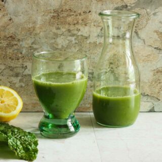 freshly pressed green juice in a glass and a carafe