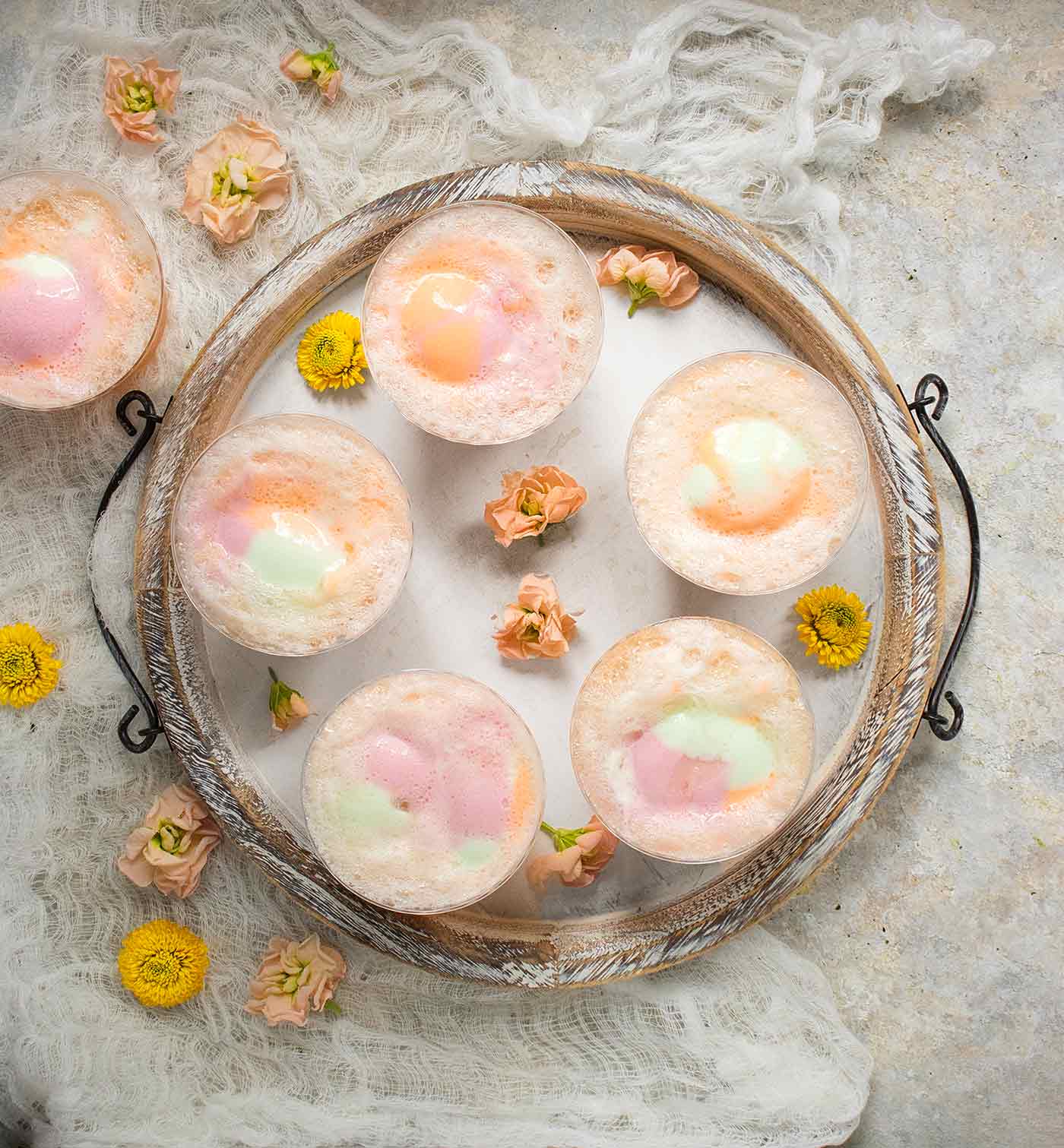Cups of party punch topped with rainbow sherbet on a white serving tray