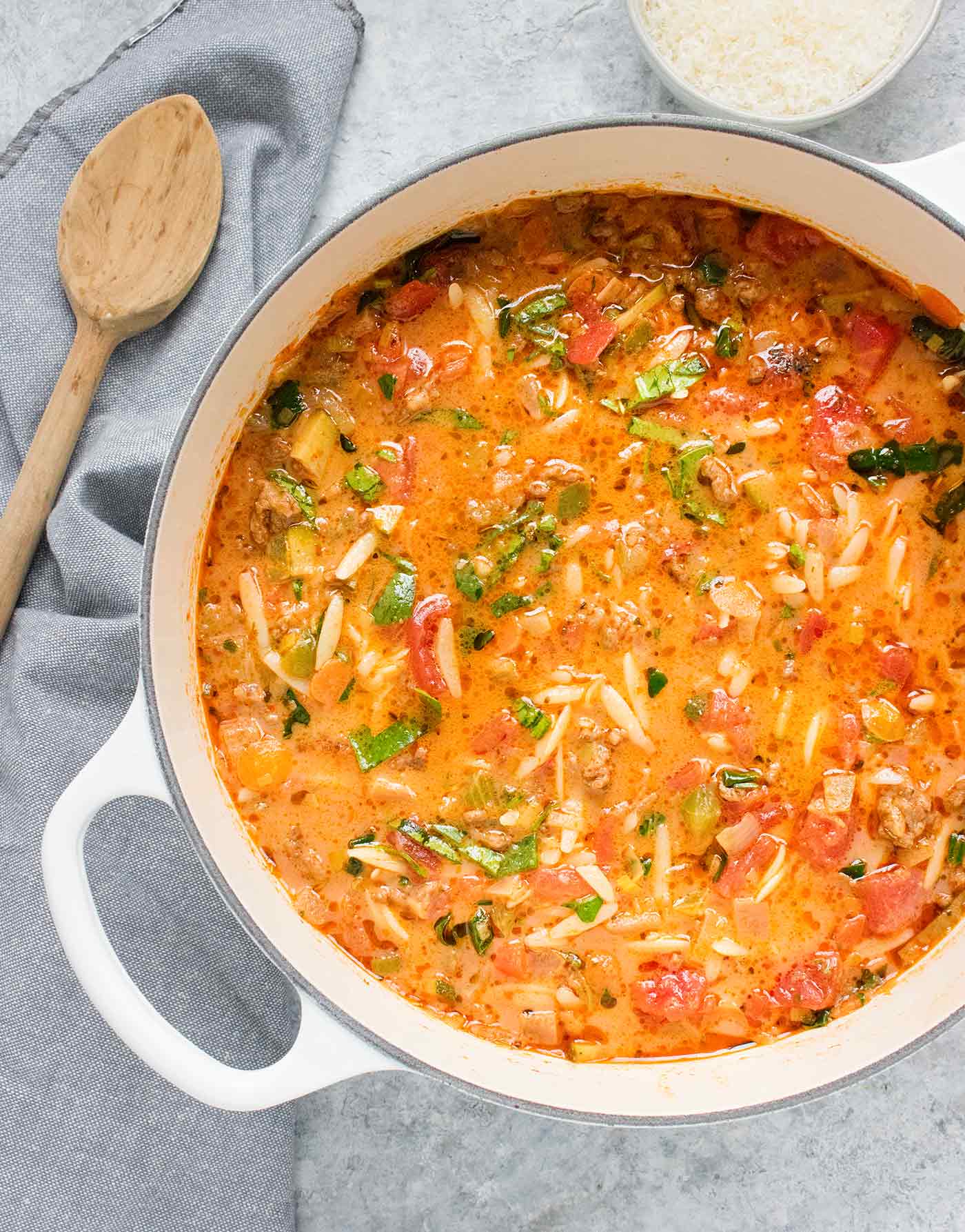 Italian Sausage Orzo Soup in a white Dutch oven with a wooden spoon