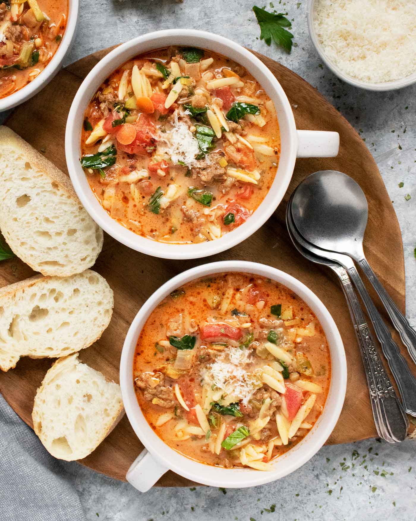 Two bowls of Italian Sausage Orzo Soup on a wooden serving tray.