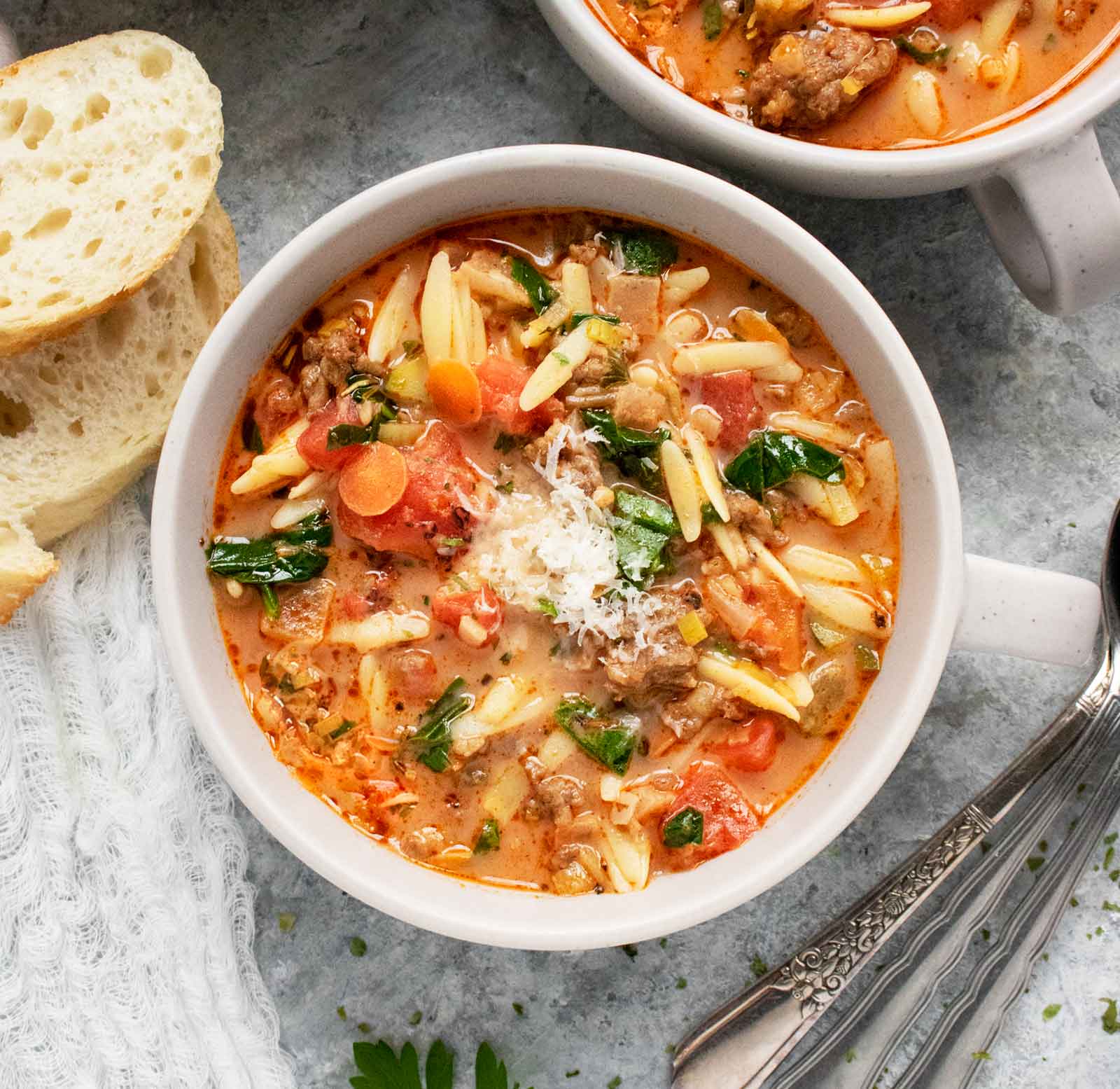 Close up of a bowl of Italian Sausage Orzo Soup with a side of bread.