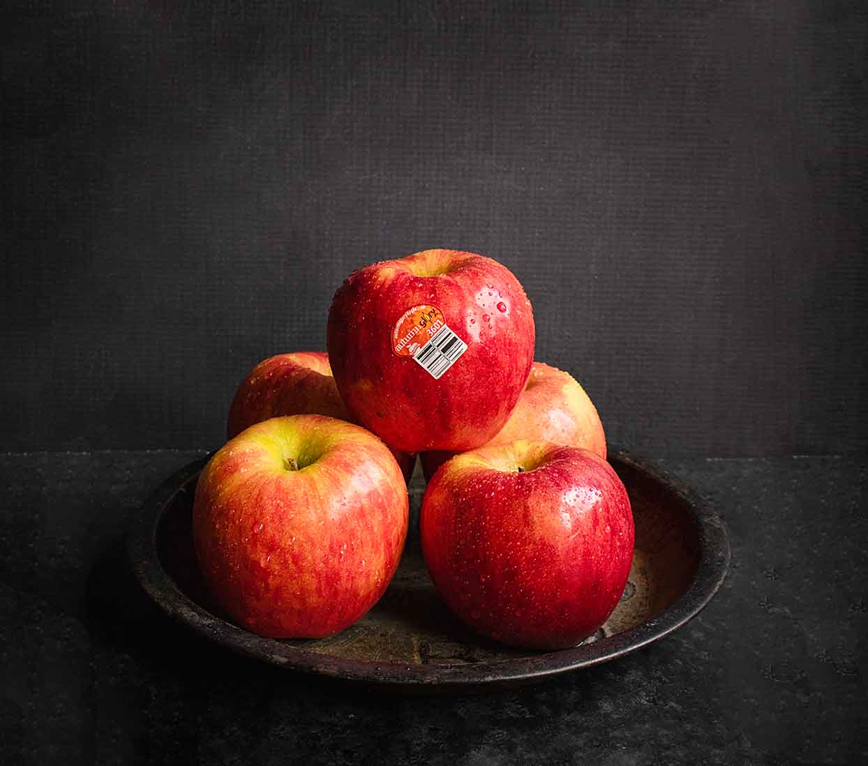Fresh Autumn Glory apples stacked in a pyramid on a rustic tin with a blackground