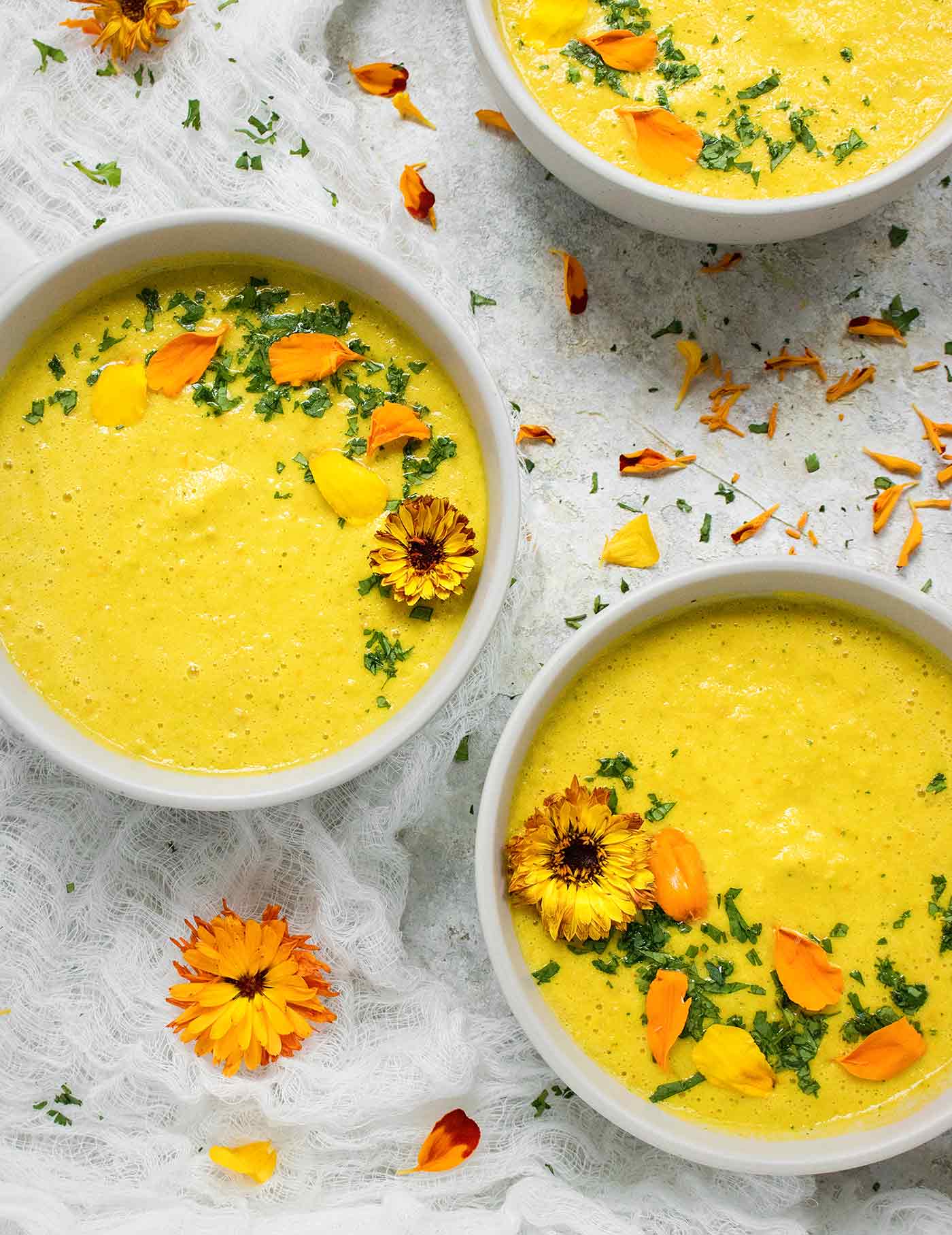 Close-up of three bowls of yellow gazpacho with edible flowers