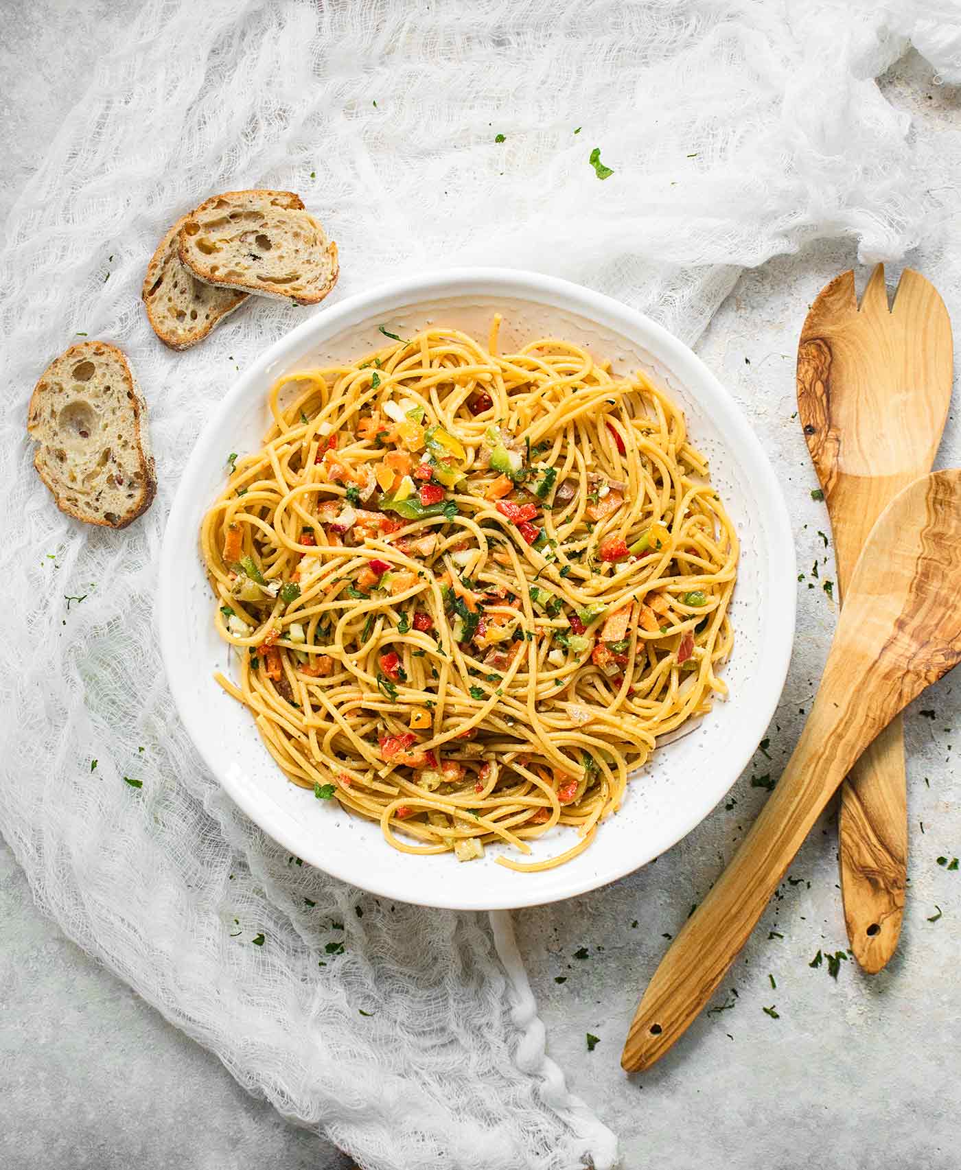 Cold Spaghetti Salad in a big, white serving bowl with wooden serving spoons on the side