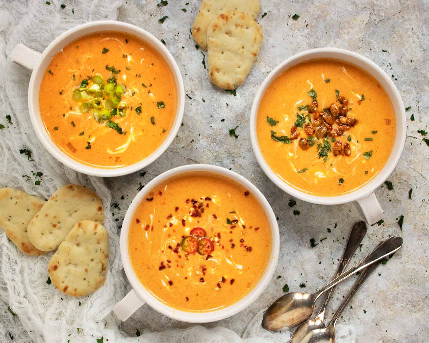 An overhead view of three bowls of Thai Pumpkin Soup with naan on the side.