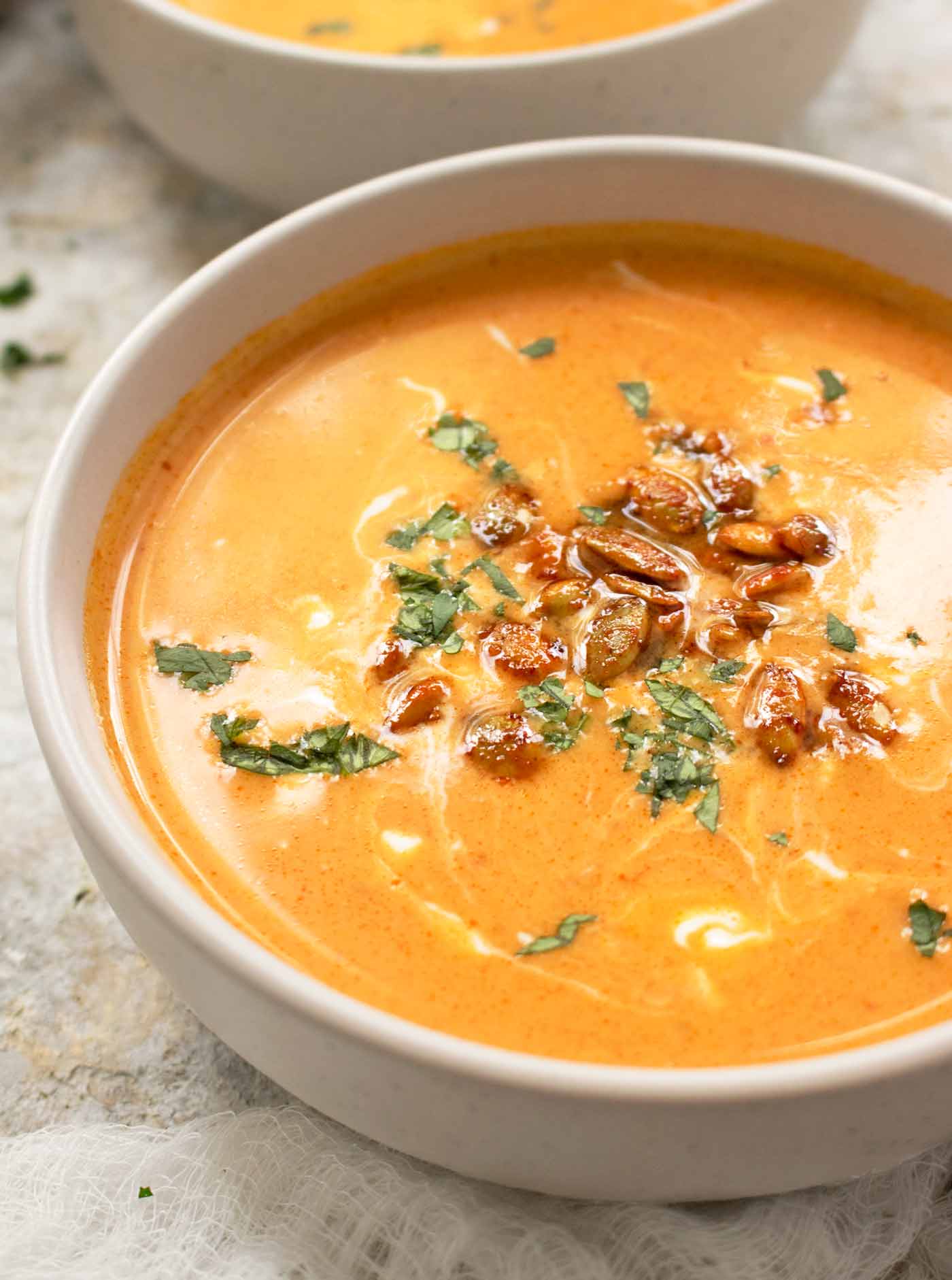 Side angled view of a bowl of Thai Pumpkin Soup, topped with roasted pepitas.