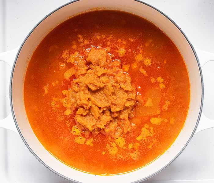 Adding the liquid and pumpkin to the pot and bringing it up to a simmer.