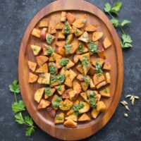 Spiced Sweet Potatoes with cilantro sauce on a wooden serving platter