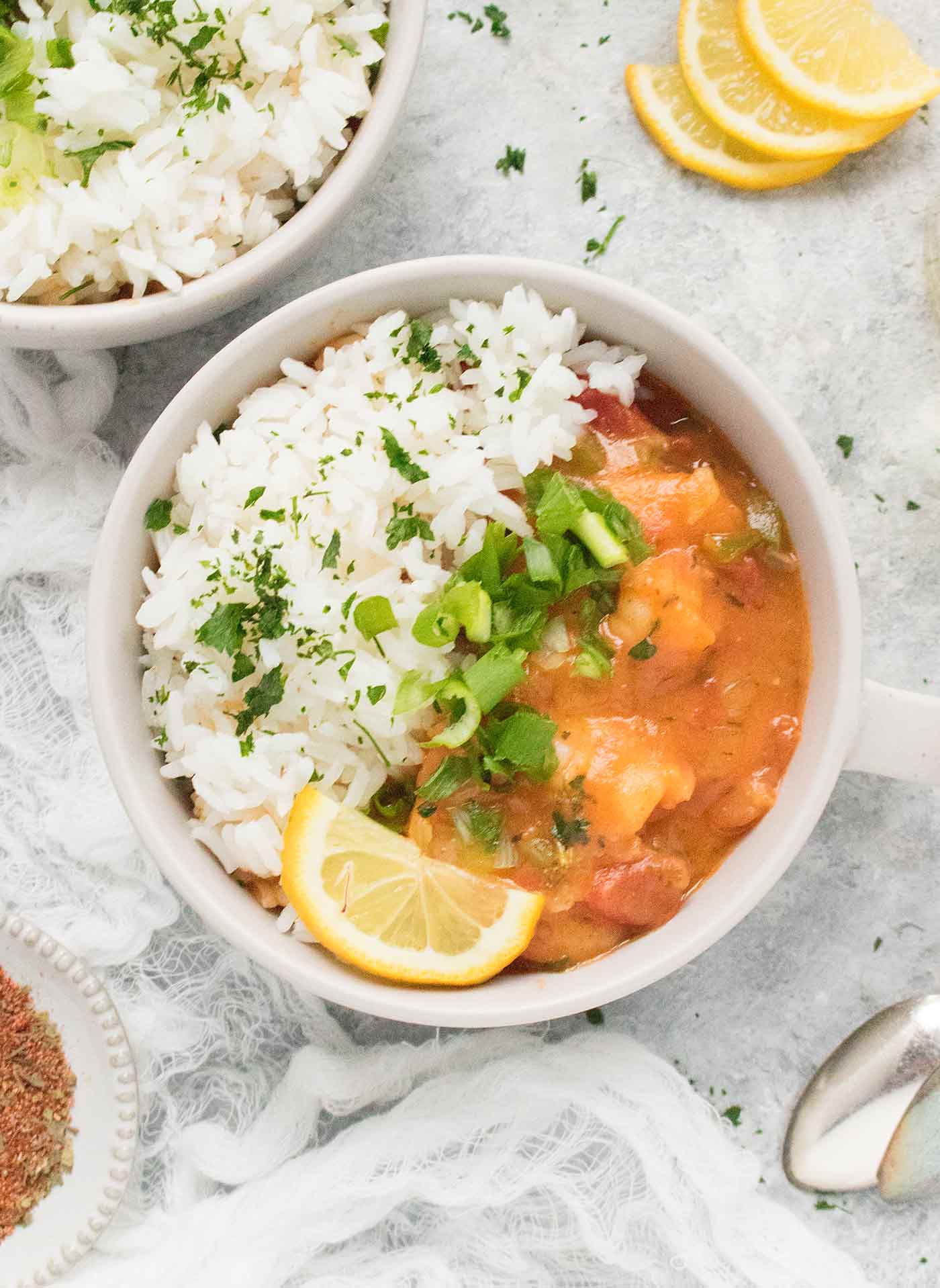 A small gray bowl with Shrimp Etouffee, white rice, and a lemon wedge.