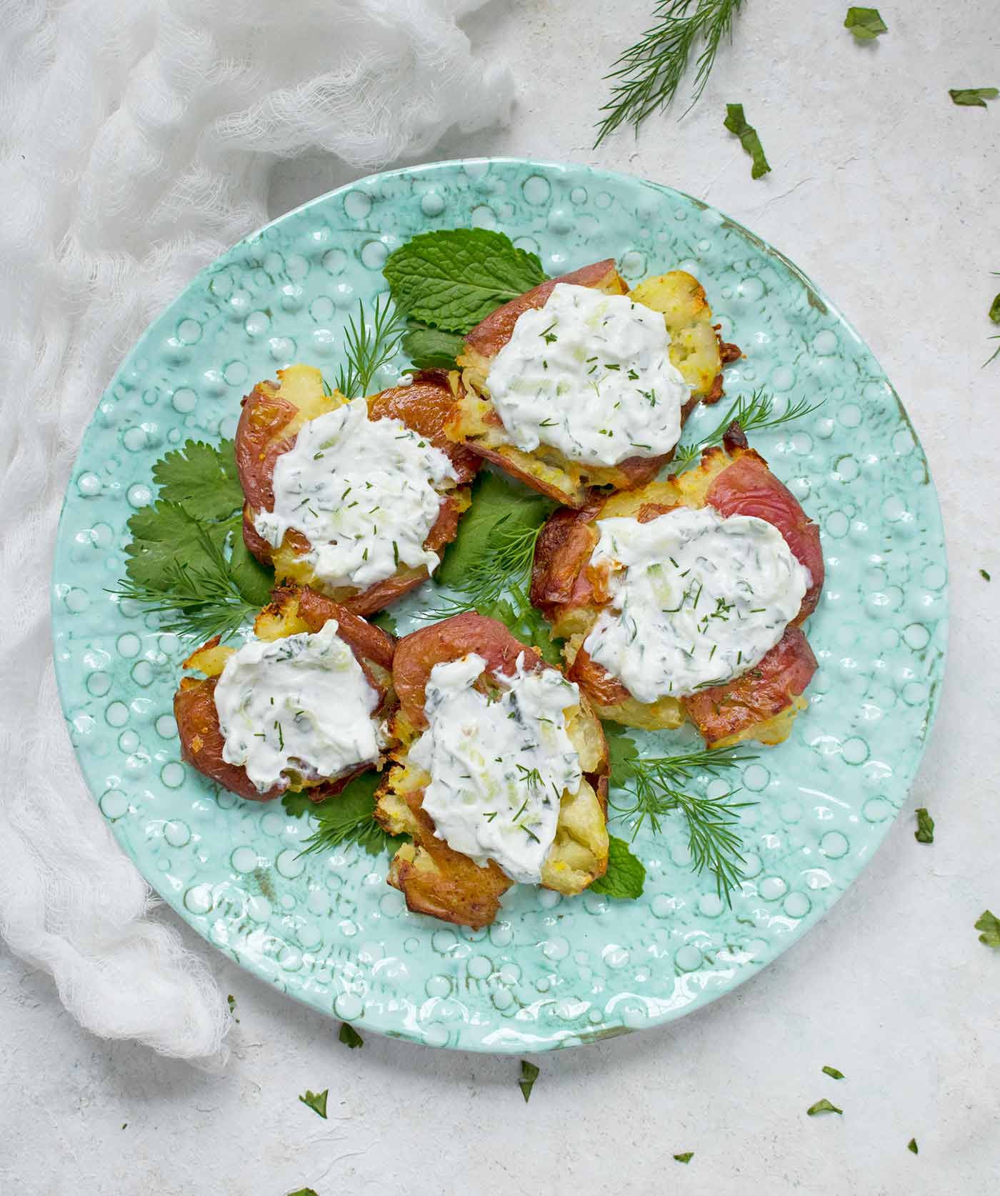Five crispy smashed potatoes topped with vegan tzatziki, on a plate