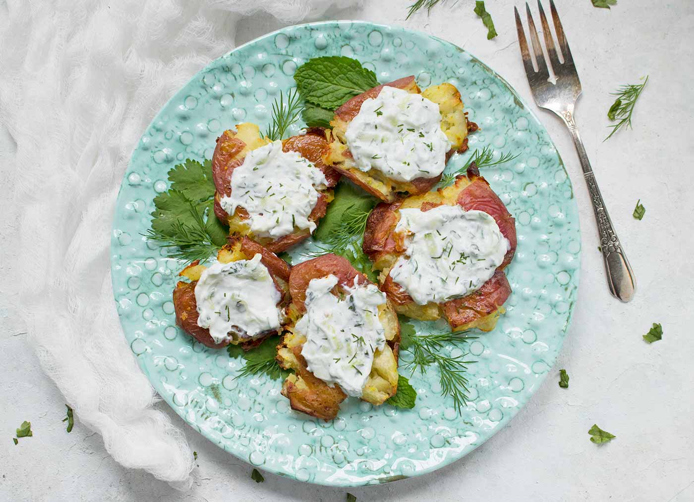 Crispy smashed potatoes topped with vegan tzatziki, on a plate