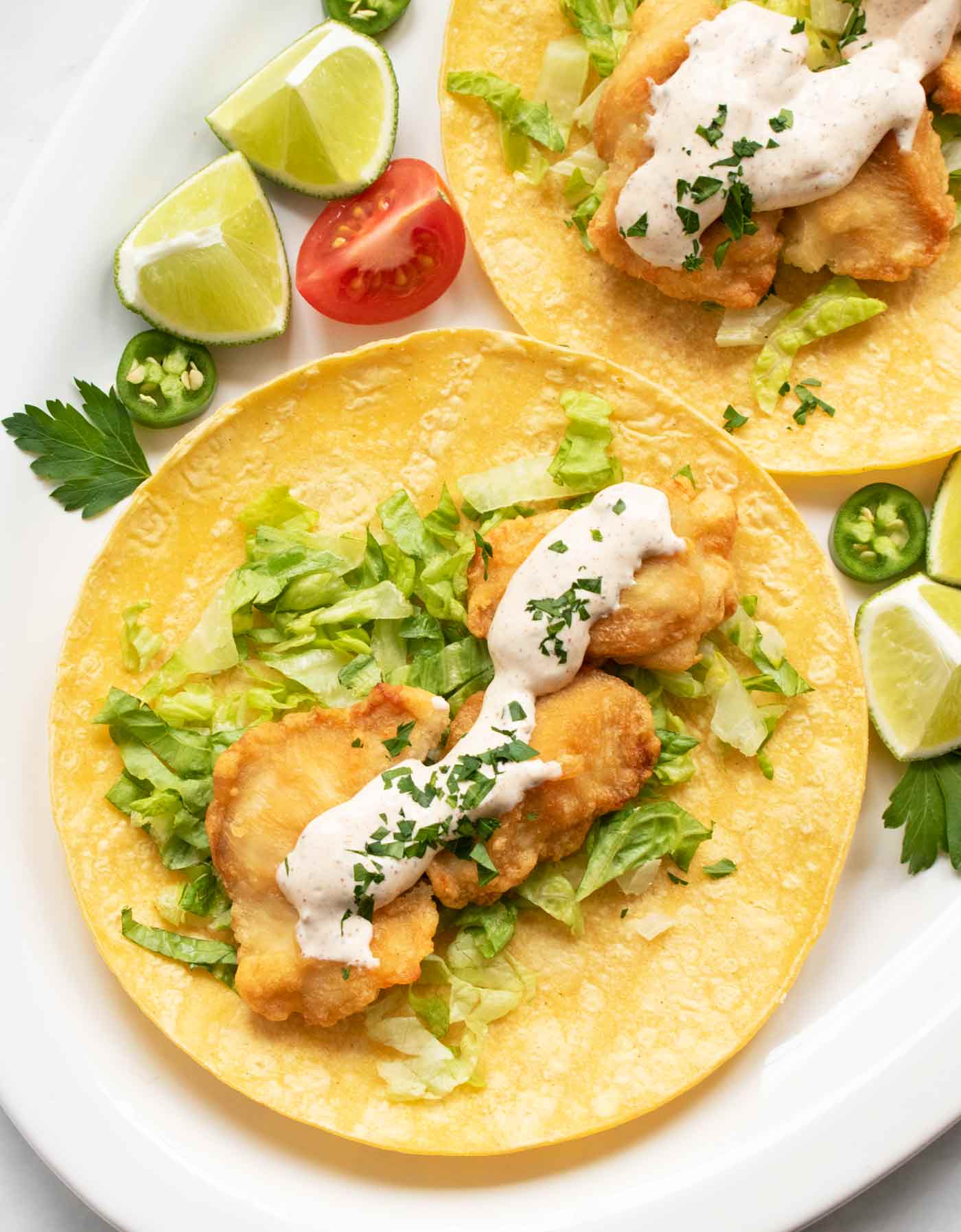 Two fish tacos with fish taco sauce on a white platter.