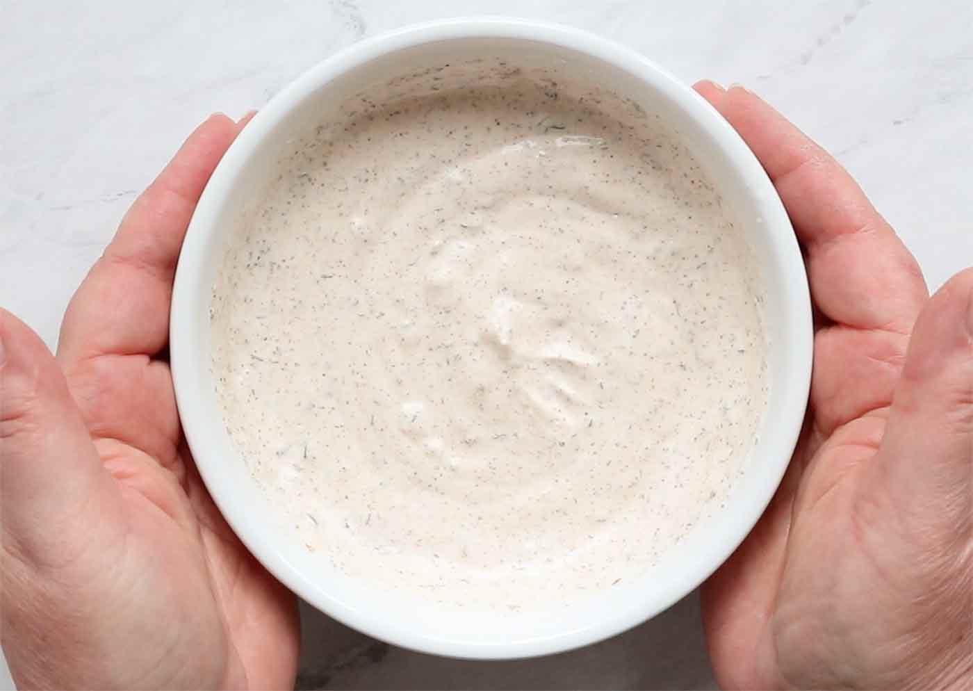 Two hands holding a bowl of fish taco sauce.