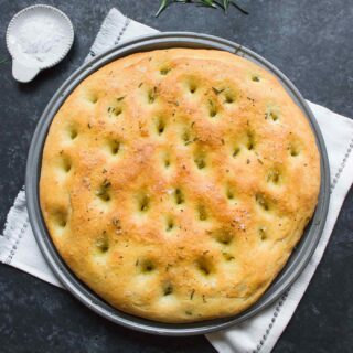 A round of freshly baked rosemary focaccia on a pizza pan