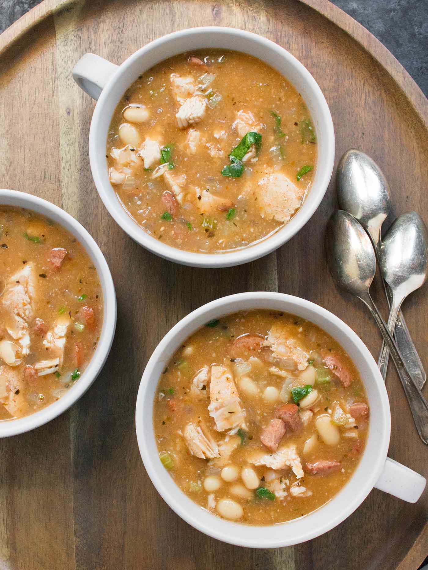 Three bowls of soup on a serving tray with spoons