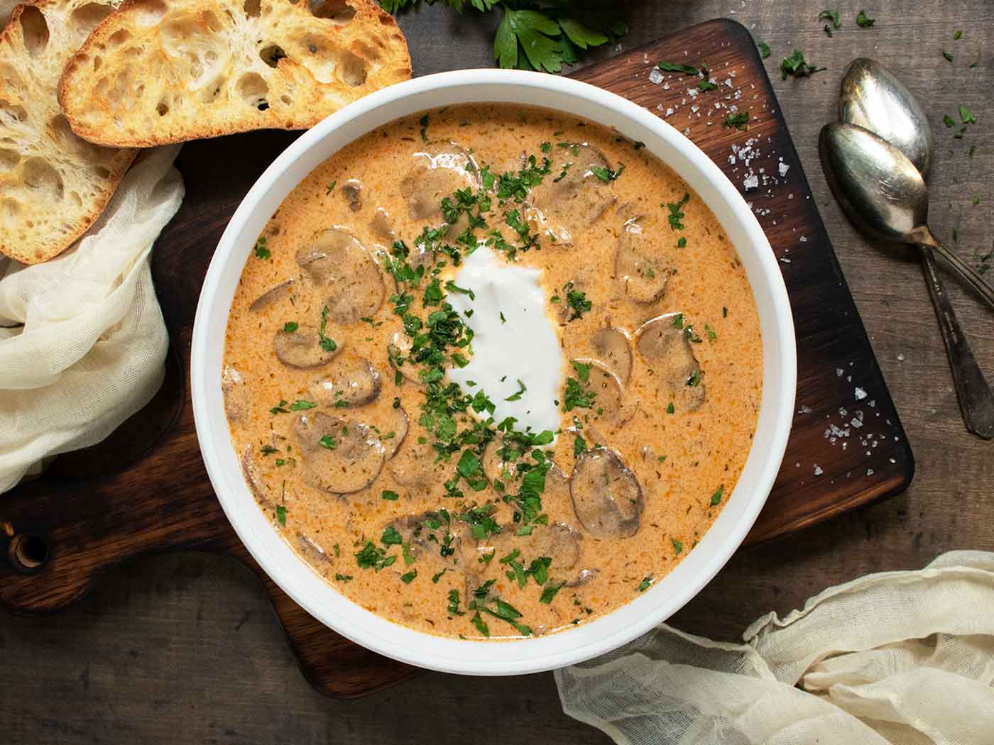 A bowl of Hungarian Mushroom Soup on a wooden board with a side of bread.