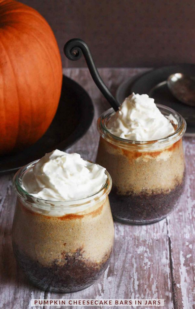 Two Pumpkin Cheesecake Bars in Jars with a pumpkin in the background.