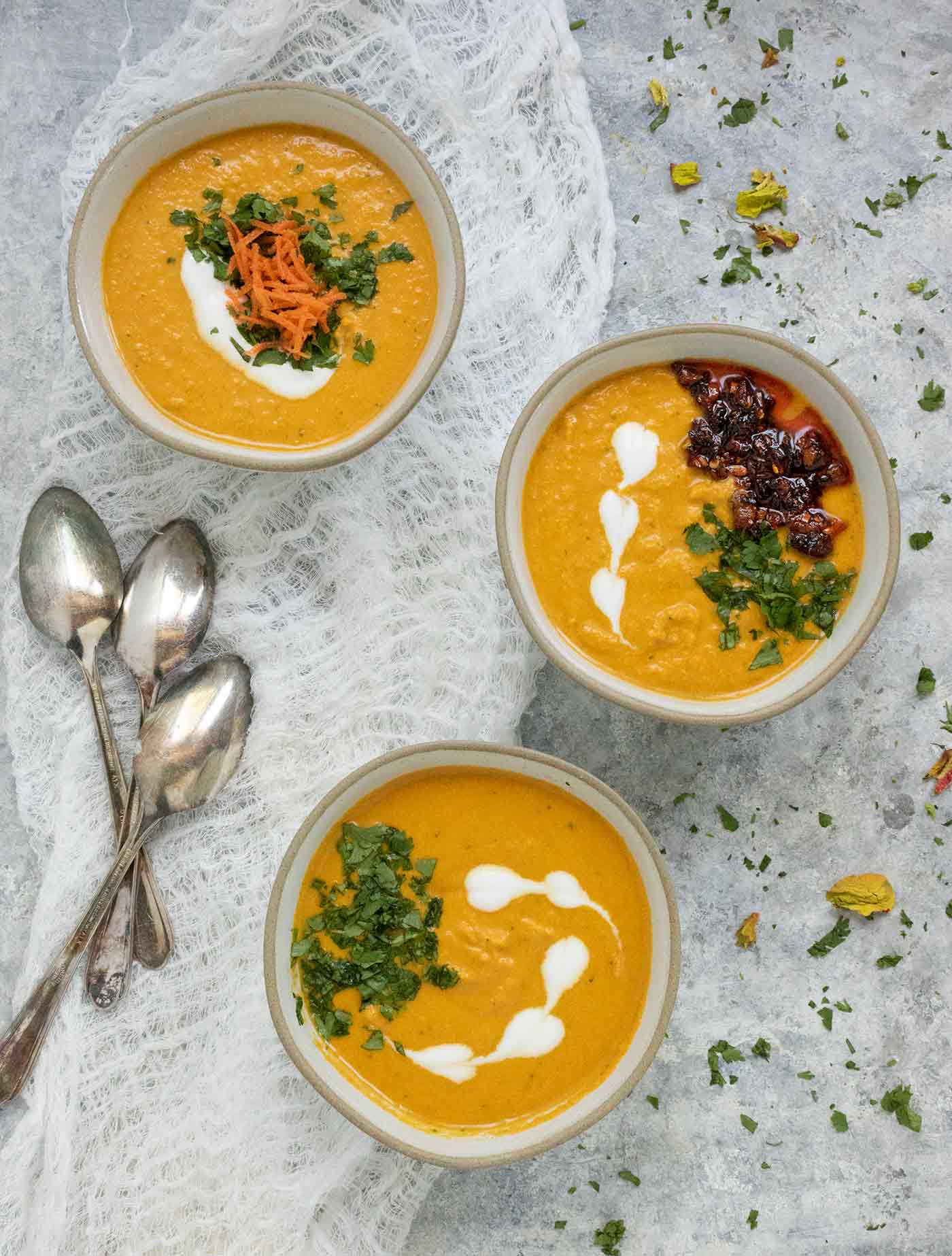 Three small bowls of carrot gazpacho with colorful garnishes.