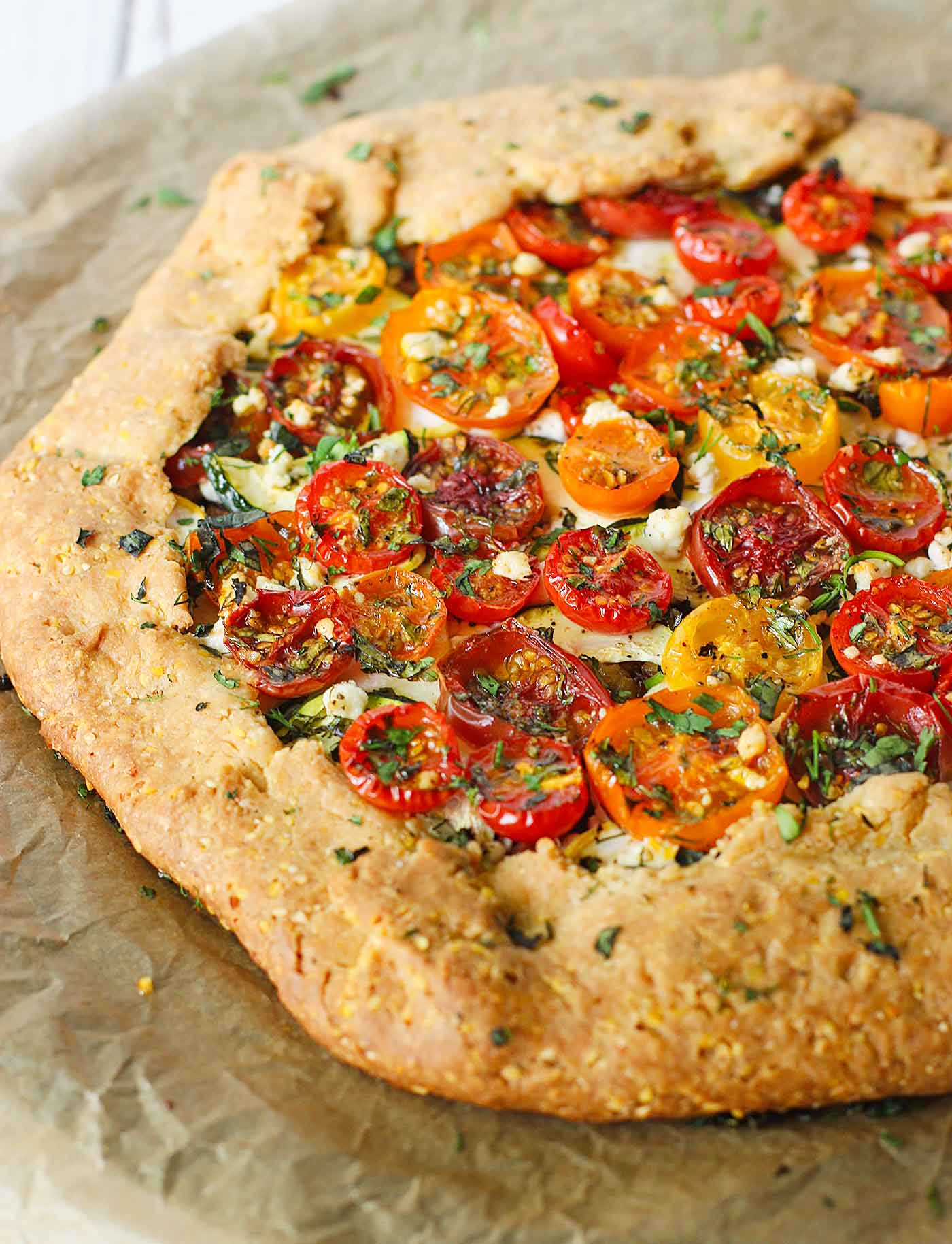 Loaded cherry tomato galette with cornmeal crust on parchment paper