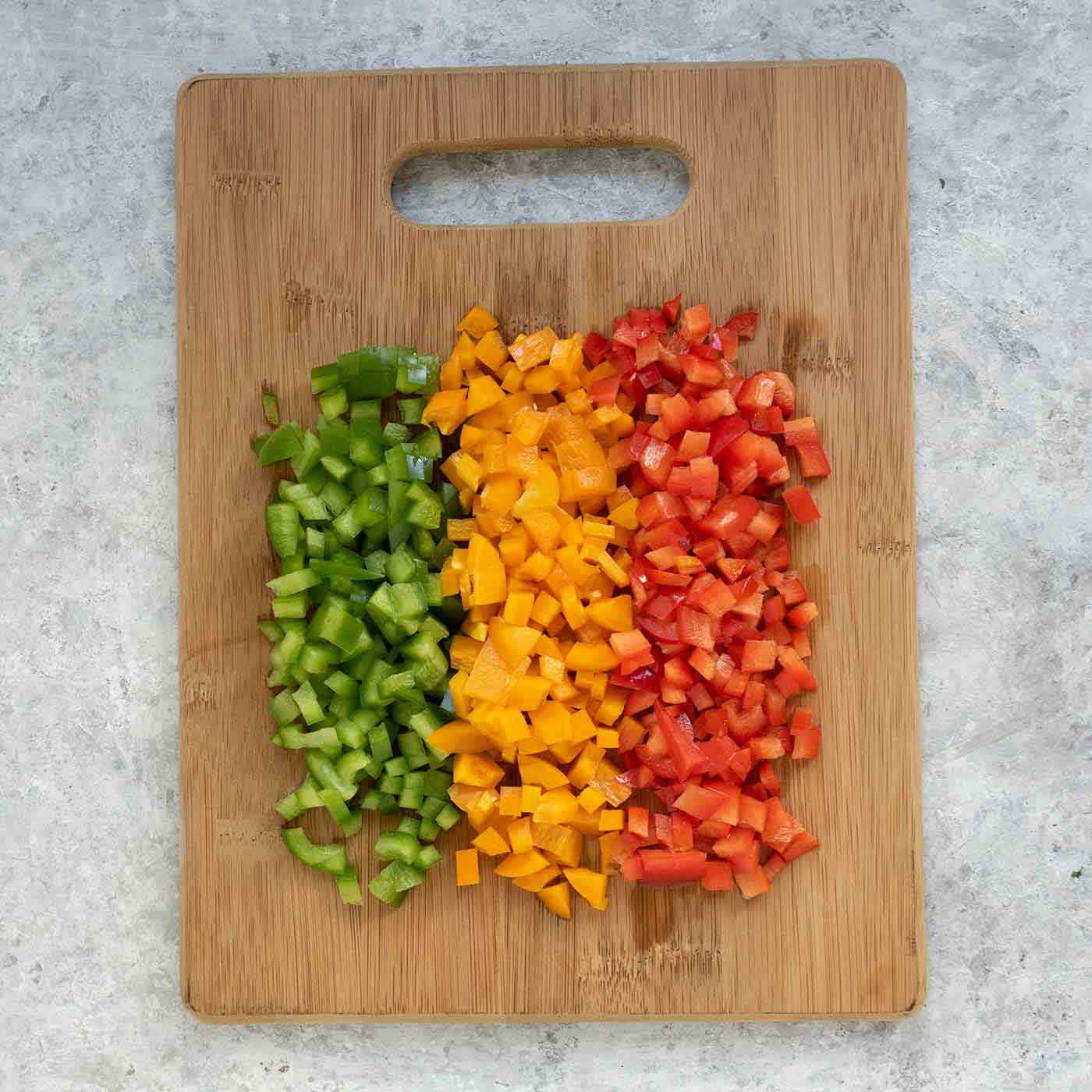 Chopped green, orange and red bell peppers on a wooden cutting board.