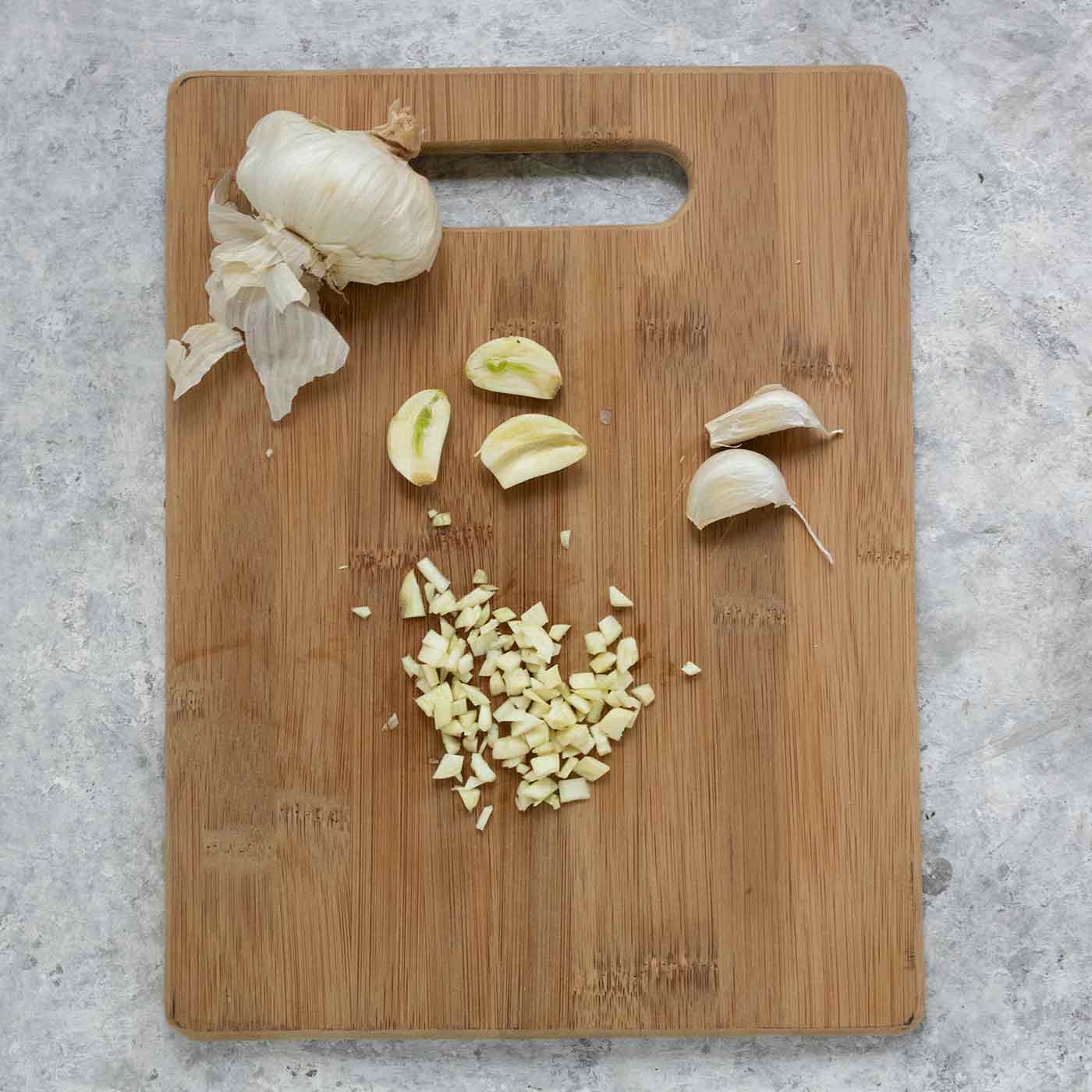 A head of garlic plus minced garlic cloves on a cutting board.