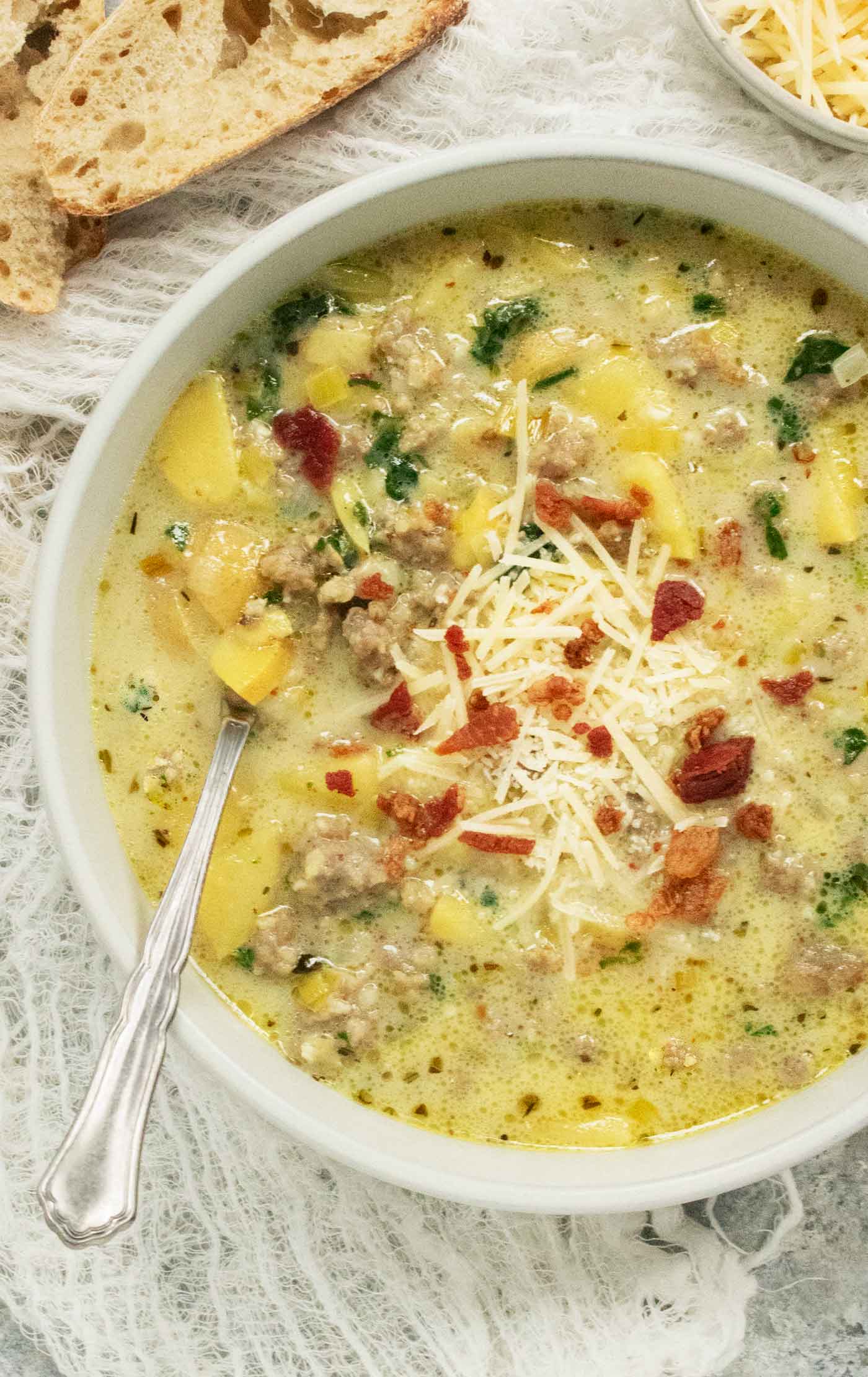 A bowl of Tuscan Potato Soup with cheese and bacon toppings, and a spoon.