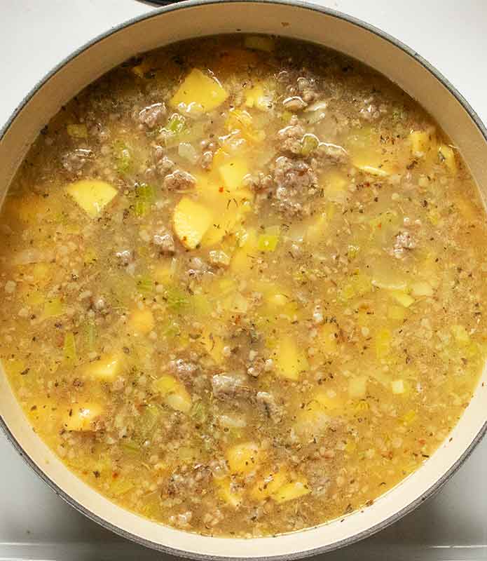 Adding the broth and potatoes to the soup.