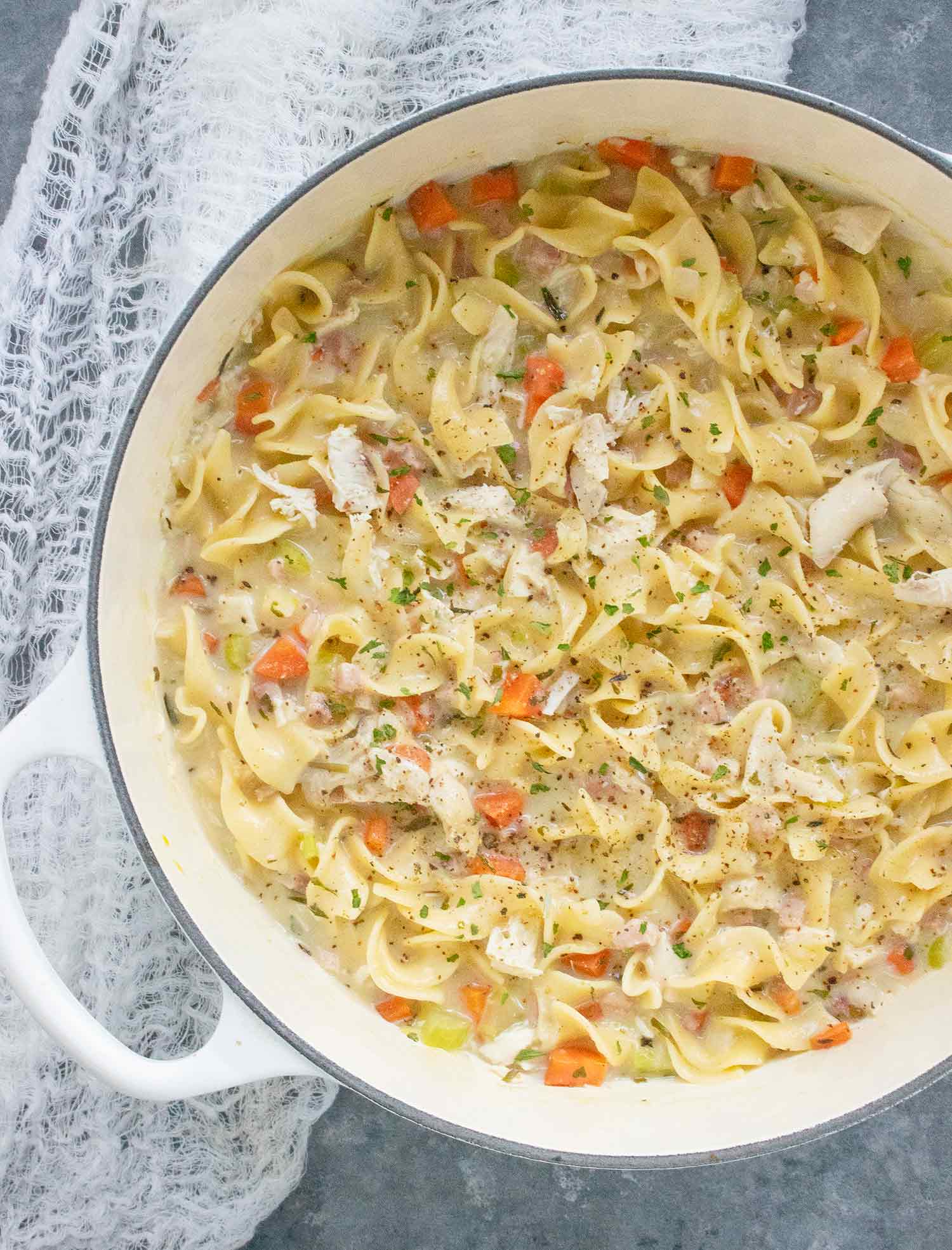 Creamy Chicken Noodle Soup with Pancetta in a white Dutch oven.