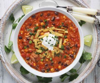 Chicken Enchilada Soup in a white bowl, served on a white wooden platter.